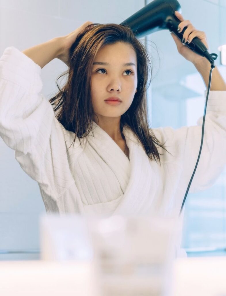 Woman blow drying roots at home after shower for healthier scalp